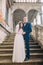 Gentle groom holding hands with his pretty bride while both stand on antique stone stairs. Full length portrait