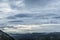 Gentle hills in gray haze on horizon. Rock ridge under sunset sky. Clouds gathered on mountain valley