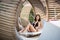 Gentle lady sitting in black bikini on original wooden lounger with white mattress among other similar sunbeds
