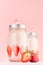 Gentle strawberry yogurts in two jars decorated sliced ripe berries with silver lids and red striped straws on soft pastel pink.