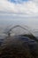 Gentle waves break over a cement structure extending into the ocean, showing the zipper effect