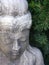 Gentle weathered cement statue of Buddha in repose framed by pine needles