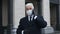 Gentleman in black gloves and coat with masked face talk on smartphone on street