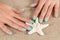 Gently female hands with a turquoise color nails polish holding starfish and sea sand in the background