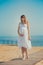 Genuine cute pregnant lady woman in white airy dress walking sand beach wooden palette bridge holding tummy abdomen. Attractive be