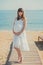 Genuine cute pregnant lady woman in white airy dress walking sand beach wooden palette bridge holding tummy abdomen. Attractive be