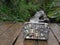 A geocache container resting on a wooden footbridge over a small flowing stream