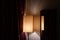 Geometry of simple lampshade reflected in mirror on wall of room with dark red ornate curtains.