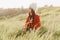 Georgian girl in white papakha and red national dress seats on the green grass and looks left side. Georgian culture