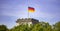 German flag waving on silver flagpole, Reichstag building in Berlin. Blue sky with clouds background