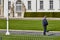 German policeman in blue uniform with white peaked cap walks in the garden in front of the Federal President`s palace patrol