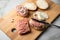 German snack bread roll buns with raw minced pork meat, butter, pepper and onion rings on wooden board and marble counter top