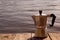 Geyser coffee maker stands on a wooden board against the background of the sea, rivers, waves, water. With copy space
