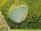 Ghost shaped drone landscape. Top down aerial view of a small pond in the middle of a forest, reflecting clouds in the sky. Bird v