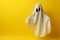 Ghostly apparition white sheet aloft against minimal yellow Halloween backdrop