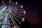 Giant Ferris Wheel with well illuminated cabins and decorated with colorful lights during night