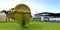 A giant molecule of gold and chromium amel in a green meadow near a futuristic estate with white walls in sunny weather. 3d