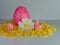 Giant pink Easter egg sitting on a bed of yellow paper shreds with a white daisy and 3 smaller pink Easter eggs on a white