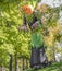 Giant pumpkin headed scary blow-up Halloween decoration tethered to ground standing among tall trees in a residential neighborhood