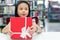 Gift box for kids girl. White box with red bow in the smiling asian girl hands for give a gift in the library, happy and surprise