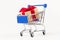 Gift box with a red bow and ribbon in a metal shiny shopping trolley on wheels on a white background