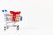 Gift box with a red bow and ribbon in a metal shiny shopping trolley on wheels on a white background