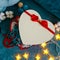 A gift box in the shape of a heart with a red bow against the background of cozy turquoise blankets framed in decorative cotton,