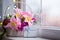 Gift box and tender bouquet of beautiful pink tulips in white basket near window with raindrops in the daylight