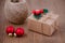 A gift box, twine ribbon and holly berries and two red baubles on brown wooden background