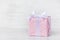 Gift box wrapped in pink dotted paper and tied satin bow over a white wood background.