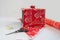 Gift box wrapped in red and white wallpaper for Christmas present packaging and materials. Scissor and scotch tape to wrap and