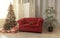 Gift boxes under Decorated Christmas tree and Red couch