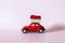 Gift by car. Red toy retro car delivering a gift on a white-pink background. Postcard for New Year, Christmas, Valentine`s Day.