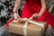 Gift for Christmas: A girl in a red dress packs a box with a gift and ties up the ribbon.