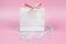 Gift in white paper shopping bag with rainbow colored candies on pink background. Sale, shopping and sweet holidays concept.