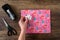 Gift wrapped with pink birthday paper, womanâ€™s hand with white bow, tape dispenser and scissors, wood table