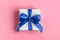 Gift wrapped in white paper with a blue bow made of satin on soft pink background