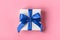 Gift wrapped in white paper with a blue bow made of satin on soft pink background