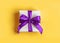 Gift wrapped in white paper with a violet bow made of satin on soft yellow background