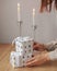 gifts in white packaging are on the table against the background of candles. a woman& x27;s hand holds a packed gift for the