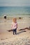 Giirl watches her brother exploring and playing in the sand with a blue bucket