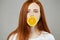 Ginger attractive girl covering her mouth with a slice of orange