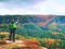 Ginger hair man takes photos with smart phone on rocky peak above autumnal valley.