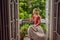 A ginger-haired woman stands on a heritage-style balcony enjoying her morning coffee. A woman in a hotel in Europe or