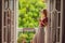 A ginger-haired woman stands on a heritage-style balcony enjoying her morning coffee. A woman in a hotel in Europe or