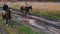 Ginger horses with equestrians on their back are galloping on the road with puddles