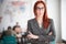 A ginger playful businesswoman in glasses standing at the office