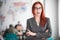 A ginger playful businesswoman in glasses standing at the office. Emotional woman showing her tongue