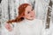 Ginger pretty girl in white sweater in winter forest. Snow december in park. Portrait. Christmas cute time.