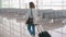 Ginger red hair woman girl at airport walking with rolling luggage suitcase bag